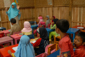 Sari mengajar di kelas berdinding kayu dan bambu, beratap seng yang bolong-bolong